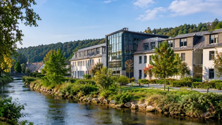 Bâtiments vitrés entourés d'arbres et de végétation au bord d'une rivière et d'une colline boisée